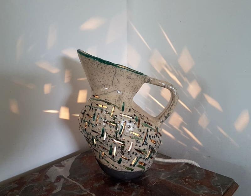 tafellamp in de vorm van een ouderwetse kan, met geometrisch lichtpatroon op de muur, door de uitsneden in het keramiek